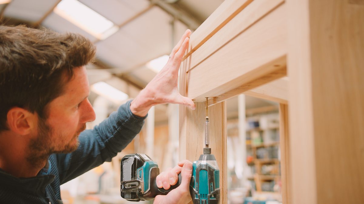 Tradesperson fitting a door frame with a power drill
